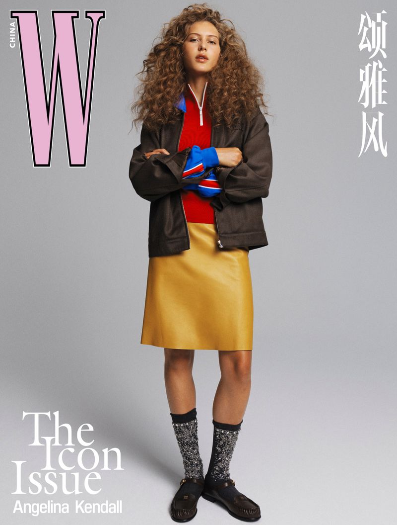 Magazine cover featuring a woman in a brown jacket and gold skirt, arms crossed, with a gray backdrop and large pink 'W' logo.