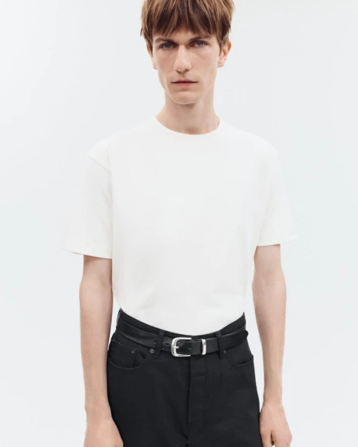 Studio shot of adult male wearing white crew neck tee shirt and black pants with belt against a white seamless backdrop.