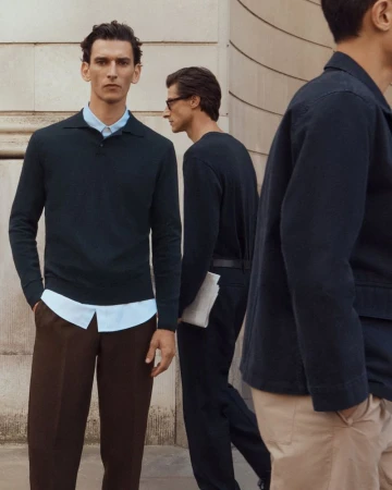 Three adult male fashion models in a neutral color palette posing outdoors on a city street in casual professional clothing.