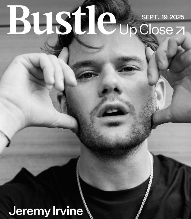 Close-up portrait of Jeremy Irvine on Bustle magazine cover, monochrome image. He poses with hands framing face. Visible text.