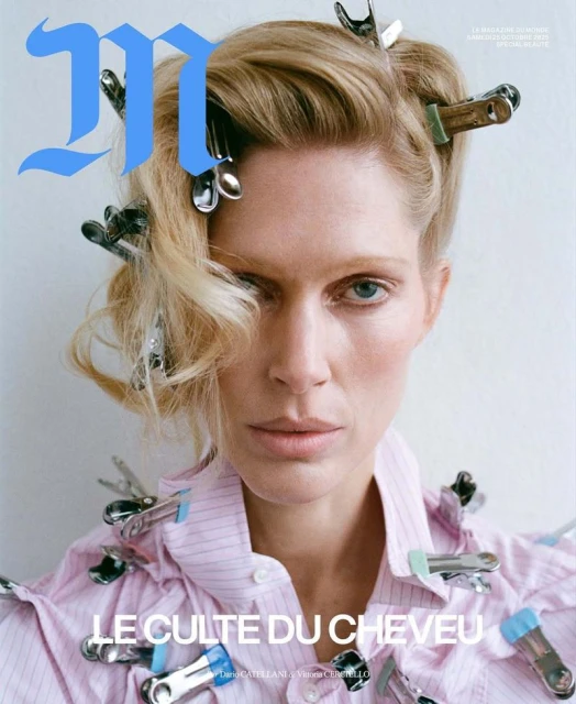 Magazine cover featuring a woman with blonde hair styled with metal clips, wearing a pink striped shirt, and a bold blue 'M' logo.