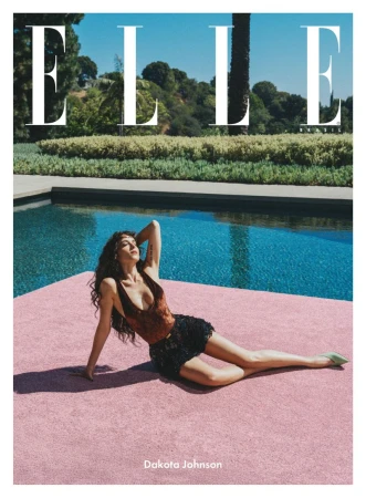Dakota Johnson reclines on pink surface next to pool for Elle magazine cover; palm trees, blue water, and green foliage visible.