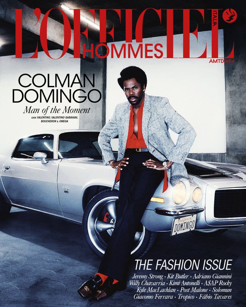 Colman Domingo cover of L'Officiel Hommes Italia, posing with a classic car, wearing a patterned blazer, dark pants, and red socks with loafers.
