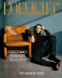 Actor Giacomo Ferrara seated on a floor next to a leather armchair against a teal wall for L Officiel Hommes Italia October 2025
