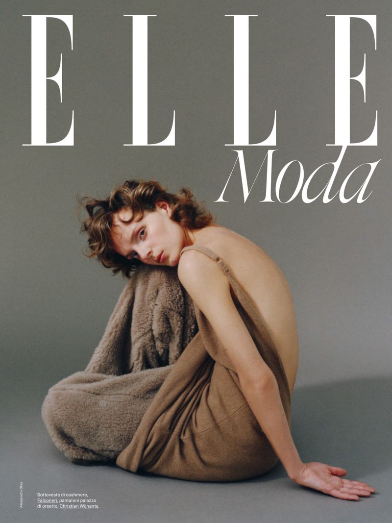 Fashion magazine cover featuring a Caucasian woman posing in a studio setting with brown dress and a neutral grey background.