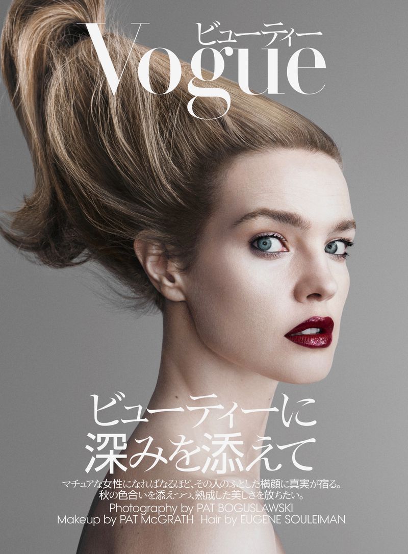 Beauty editorial shot of a young adult woman with blonde hair in a ponytail, wearing dark lipstick, against a gray background.