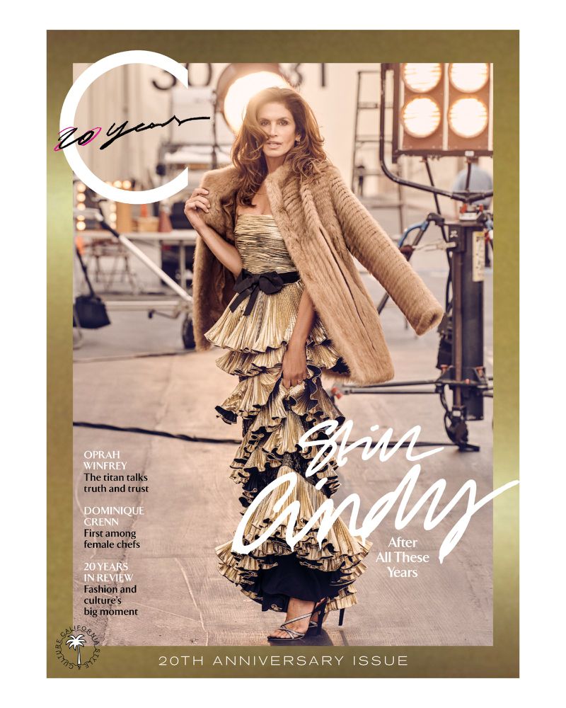 Magazine cover featuring a woman in a gold dress and fur coat, posing in a studio with stage lights and equipment in the background.