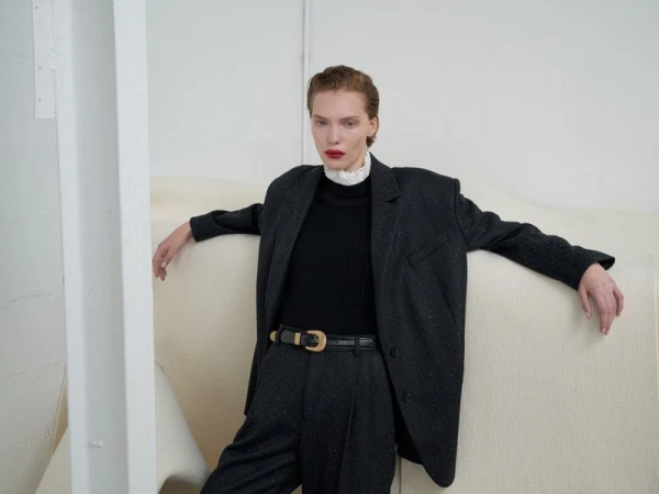 Model in oversized dark grey blazer and matching trousers leaning against a white studio wall for Sandro Fall/Winter 2024