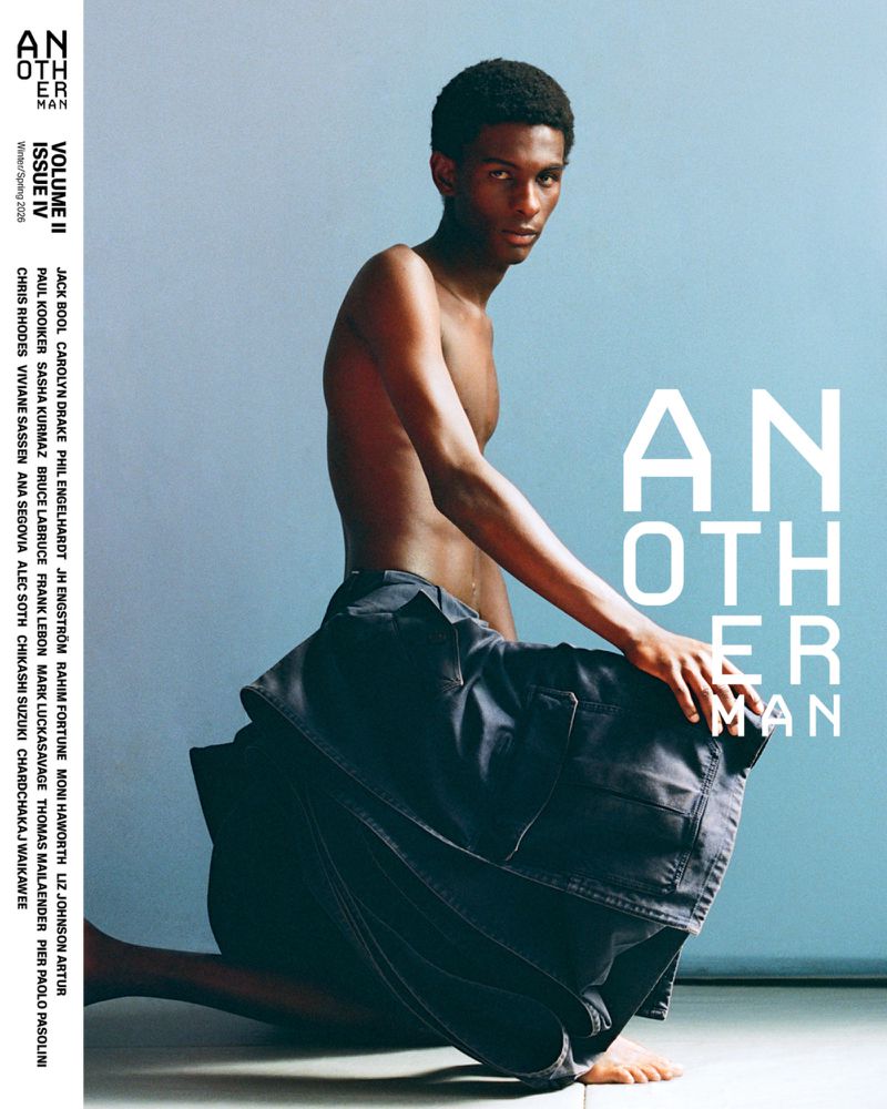 Striking magazine cover shot featuring a bare-chested Black male model kneeling with dark blue trousers, against a pale blue backdrop.
