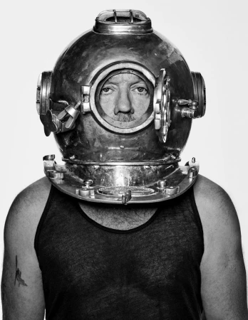Michael Stipe wearing a vintage brass diving helmet and dark tank top against a plain white background
