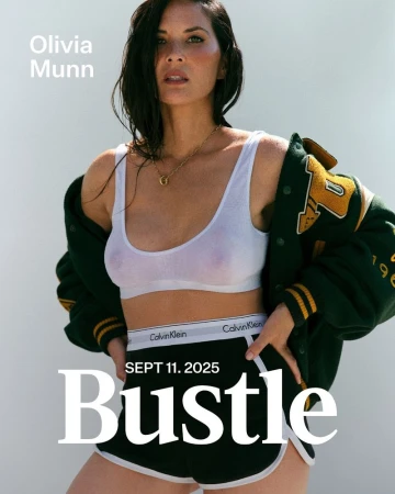 Olivia Munn poses in a sporty casual outfit consisting of a white tank top, Calvin Klein underwear, and black athletic shorts, indoor.