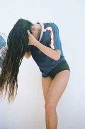 Olivia Munn with long wet hair bending forward wearing blue top and dark briefs in Bustle Magazine editorial