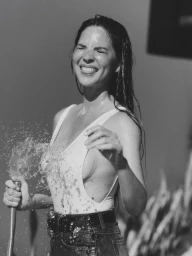 Monochrome portrait of Olivia Munn laughing with eyes closed while spraying water from a hose for Bustle Magazine.