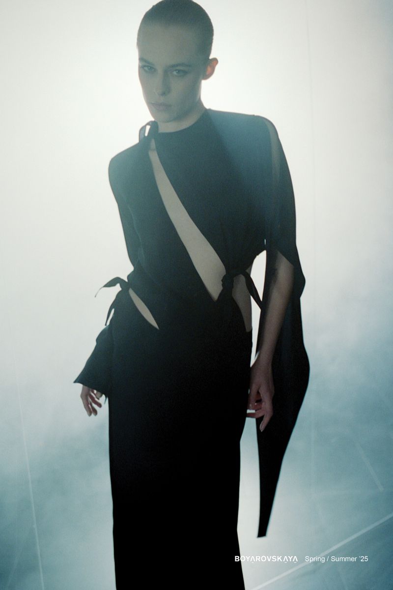 Fashion model in a black dress with cutouts poses against a soft, bright background in a studio fashion photography setting.