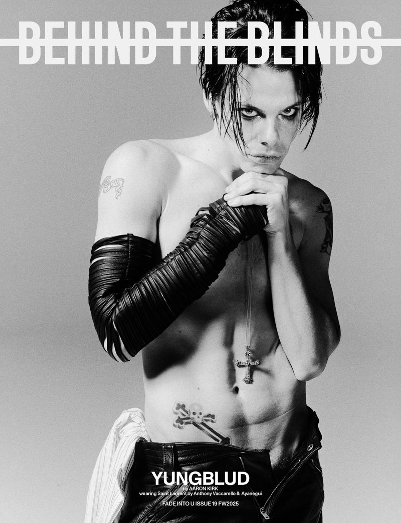 Black and white portrait of musician YUNGBLUD with hands clasped beneath his chin wearing leather gloves and a cross necklace.