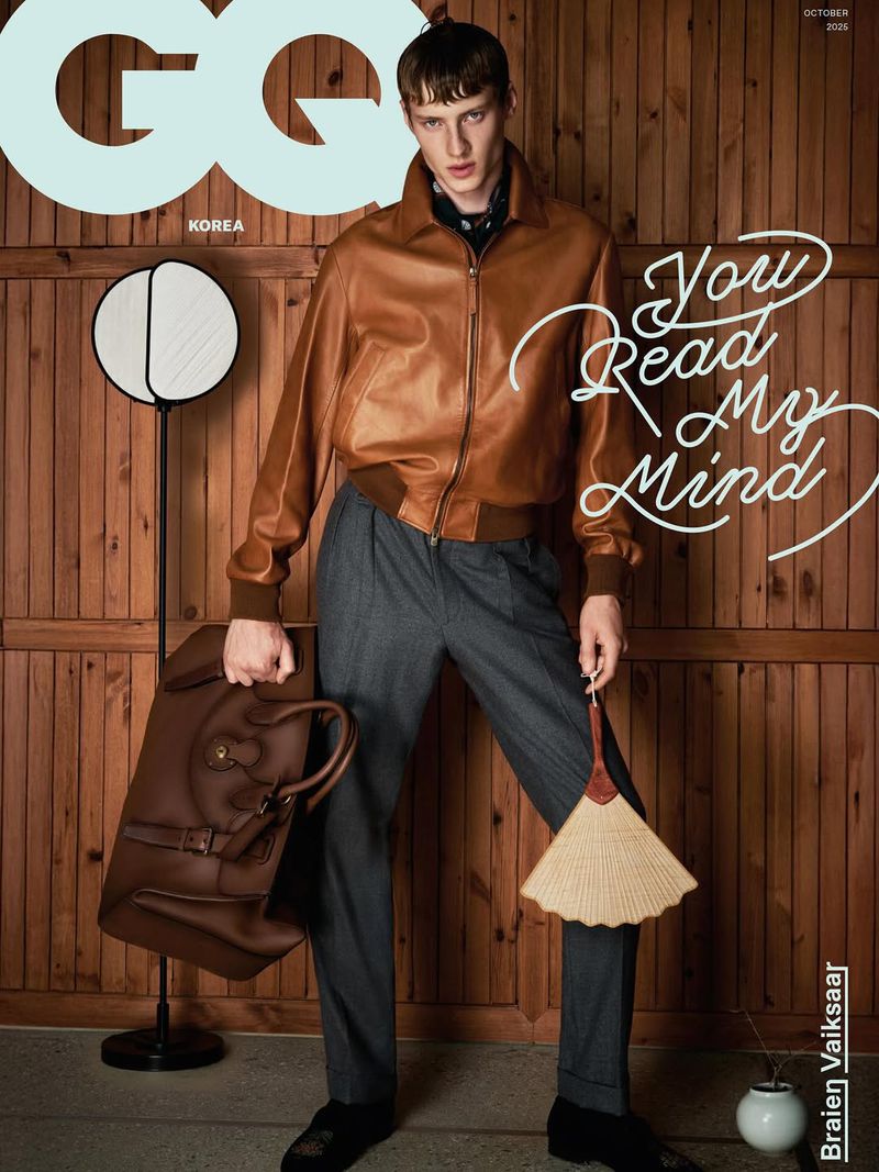 GQ Korea cover featuring a male model in a brown leather jacket and grey pants holding a handbag and fan in a wooden set.