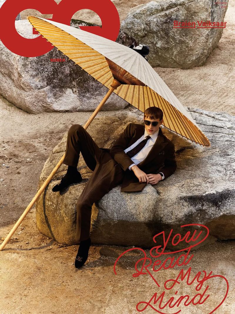 GQ cover featuring a man in a brown suit lounging on rocks under an umbrella, exuding a relaxed editorial fashion vibe outdoors.