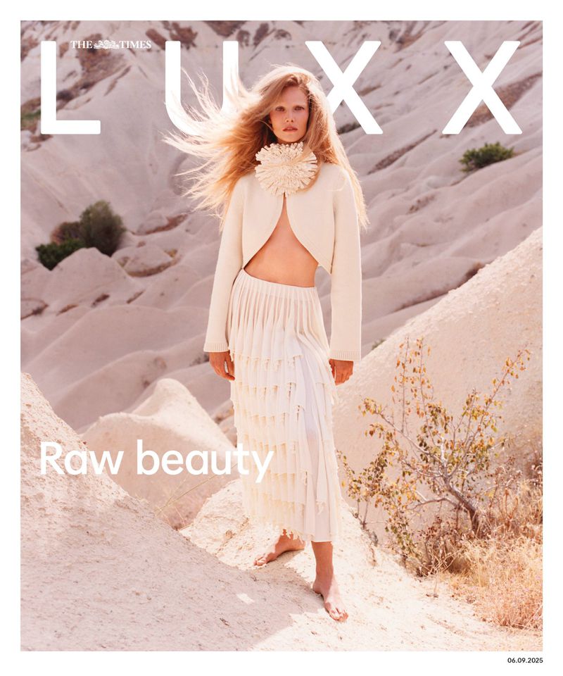 Fashion magazine cover featuring a model in a white skirt and jacket, standing outdoors against a desert backdrop, with 'LUXX' printed on the cover.