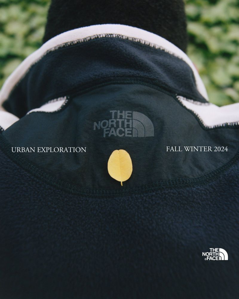 Close-up of black fleece jacket with The North Face logo and a single leaf, showcasing outdoor urban exploration fashion in a natural setting.
