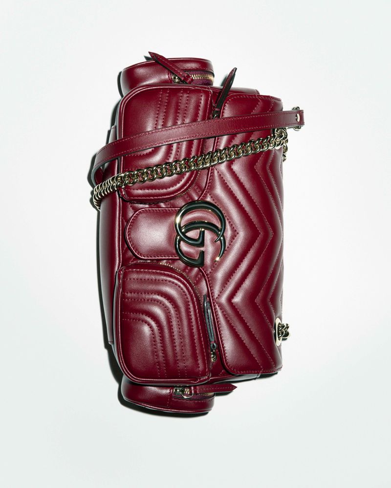 Studio shot of a burgundy leather Gucci Marmont backpack with chevron quilting, gold chain strap, and metal GG logo on a white background.