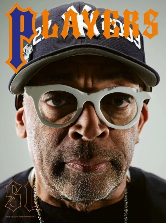 Close-up portrait of Spike Lee wearing a baseball cap and white-framed glasses, showcasing his distinctive style and personality.