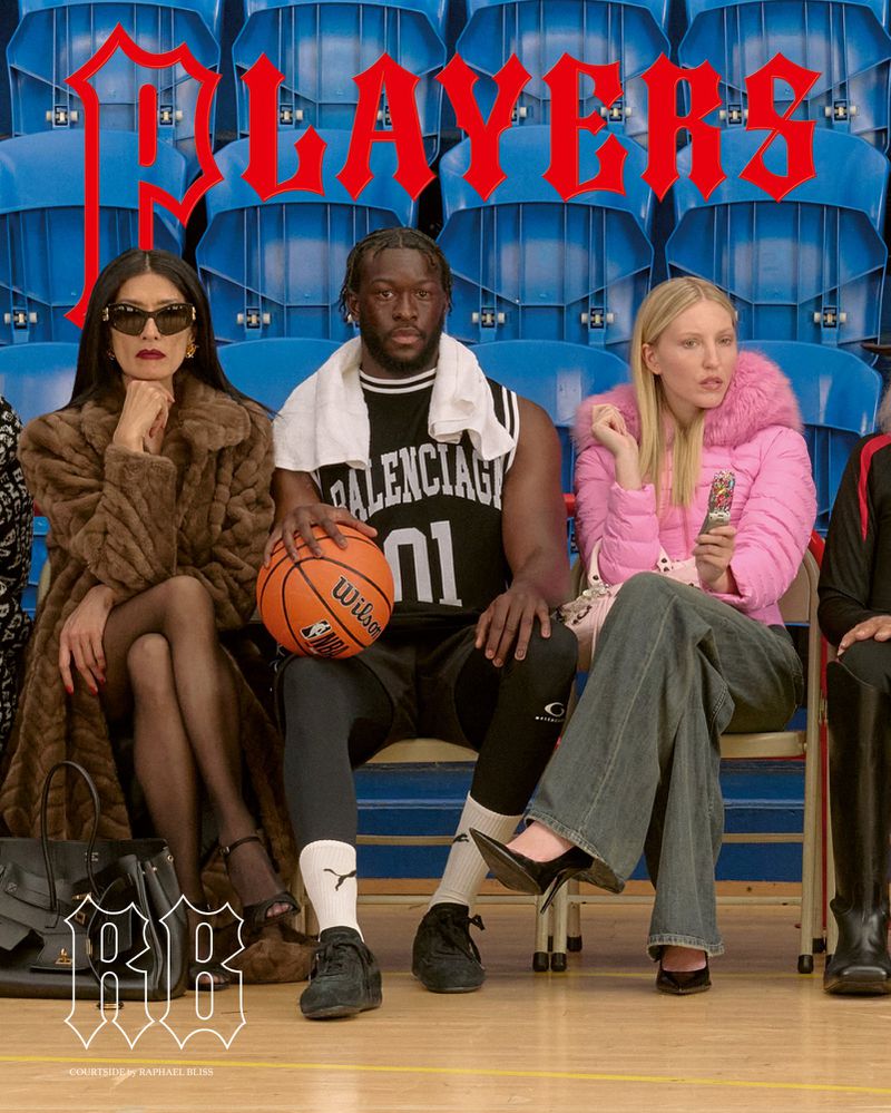 Three people sit on blue bleachers in a basketball arena. A man in a Balenciaga jersey holds a Wilson basketball.