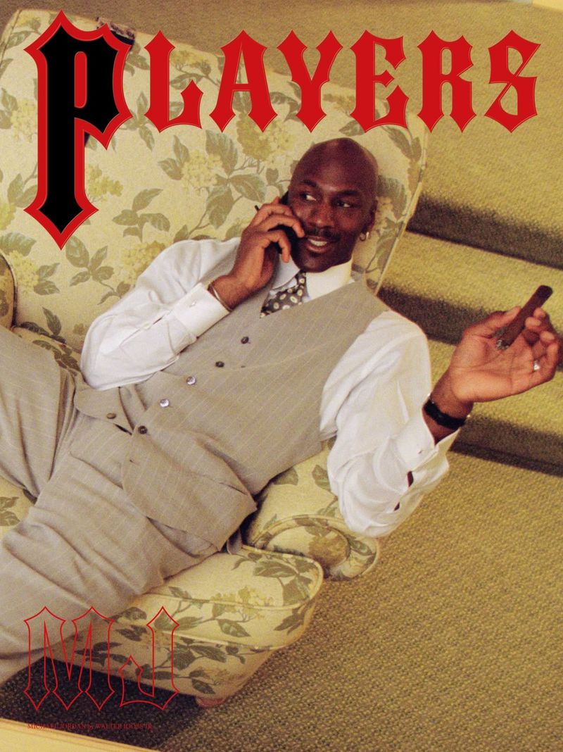 Michael Jordan lounges with a cigar and a phone in a floral armchair, wearing a gray suit with the word 'Players' in the backdrop.
