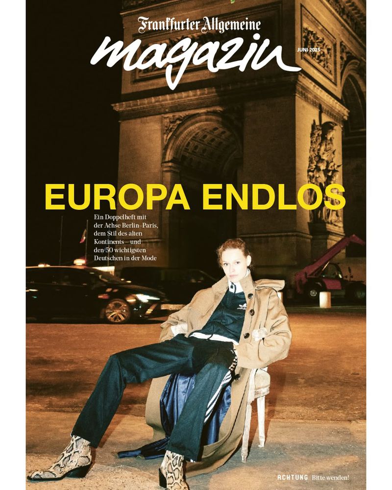 Magazine cover featuring a person seated in front of the Arc de Triomphe at night. They are wearing boots, pants, and a trench coat.