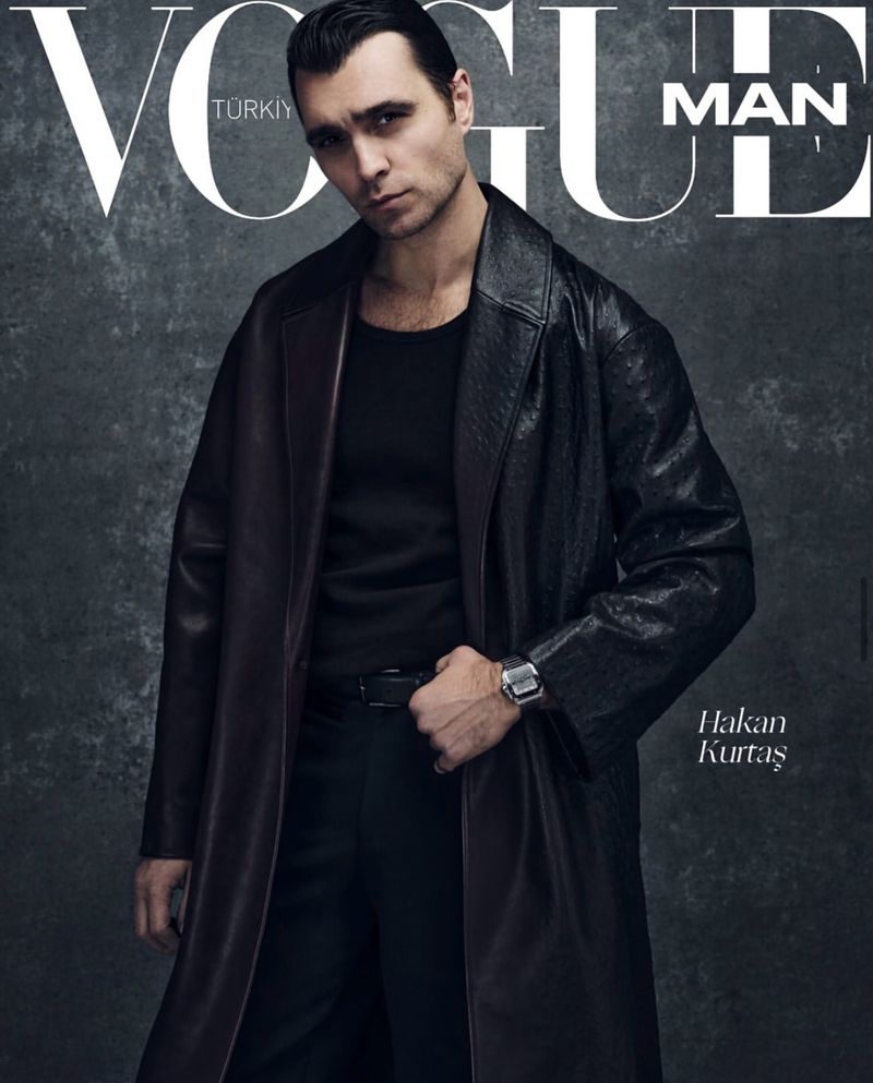 Vogue Man cover featuring a handsome man in a long leather coat and black shirt, posing against a textured grey background.