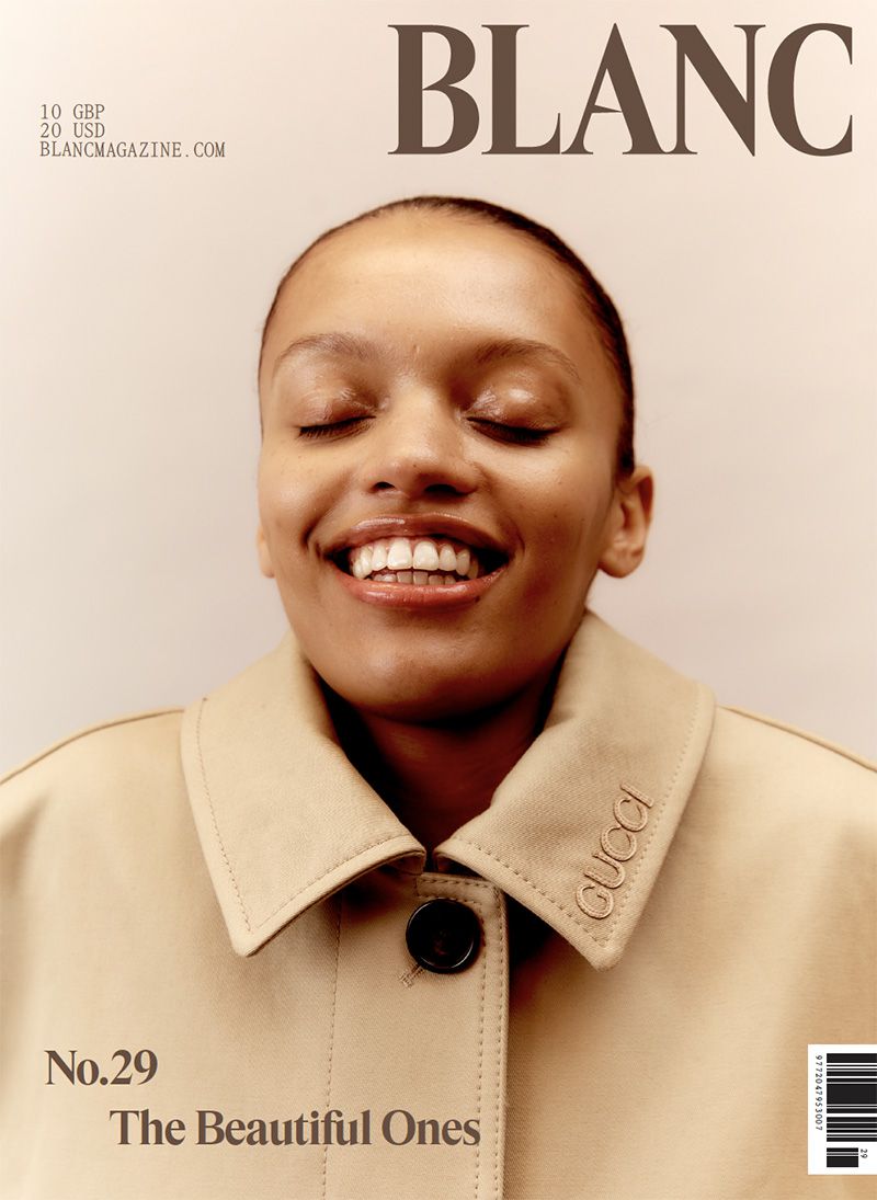 Blanc Magazine cover featuring an adult woman smiling with her eyes closed, wearing a tan-colored trench coat with Gucci branding.