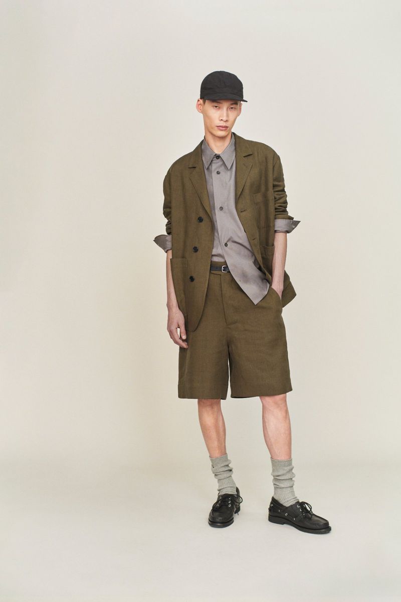 Male fashion model poses in a blazer and shorts outfit, complete with cap, socks, and shoes, against a neutral studio backdrop.