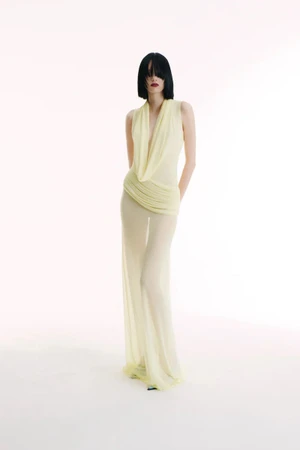 Model in sheer pale yellow draped dress with black bob haircut against a bright white background