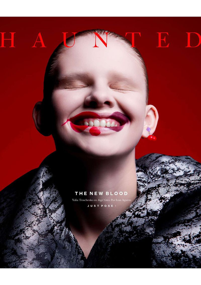 Close-up portrait of a smiling child with smeared lipstick, eyes closed, against a red background, wearing a patterned jacket.