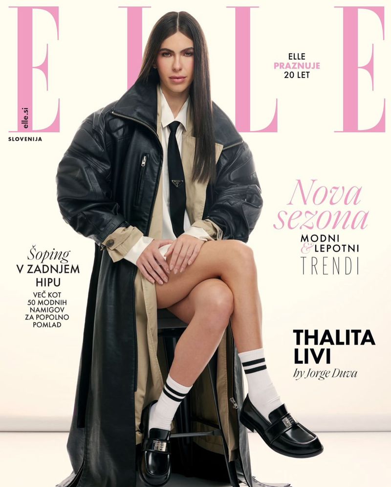 Fashion magazine cover featuring a woman in an oversized black jacket, white shirt, and black tie, seated with legs crossed, wearing white socks and black loafers.