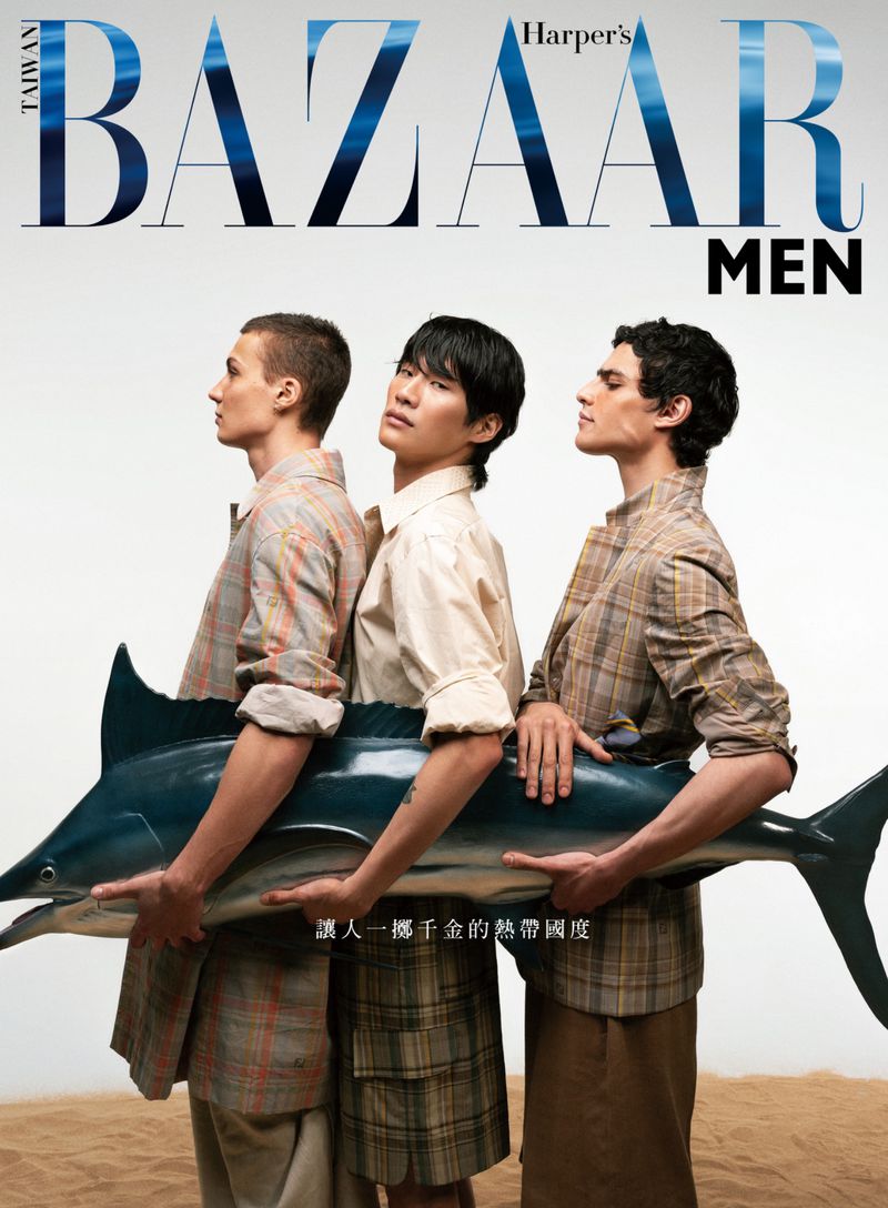 Magazine cover featuring three adult males holding a large blue marlin fish, wearing light-colored shirts, on a sandy backdrop.
