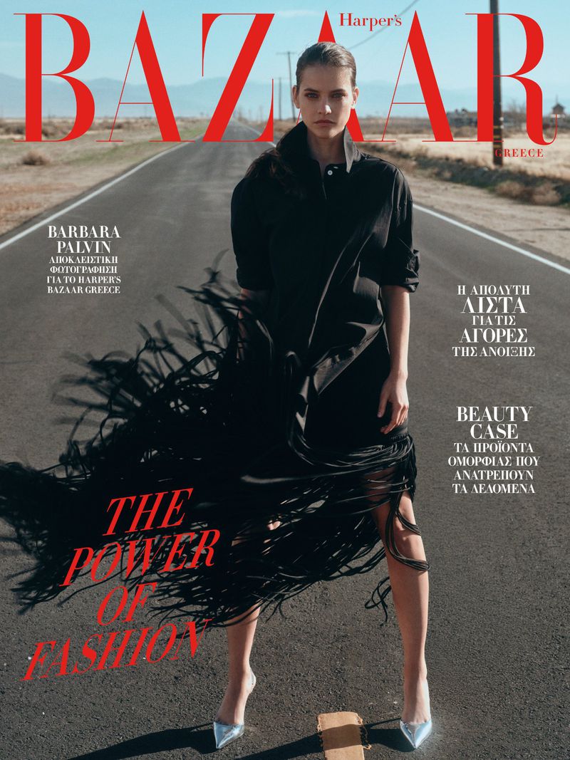 Harper's Bazaar Greece cover features a woman in a black fringed dress posing on a desert road with mountains, magazine masthead.