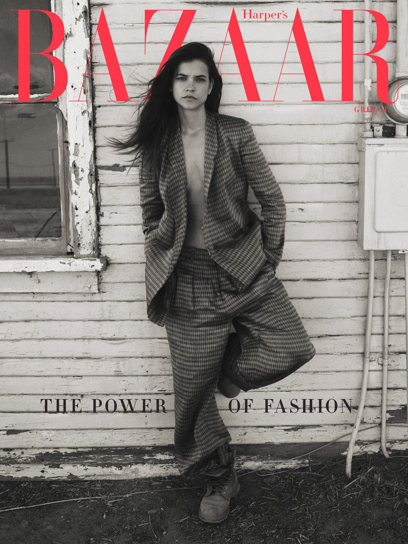 Harper's Bazaar cover with a young woman in a suit, standing in front of a weathered white building, styled for high fashion.