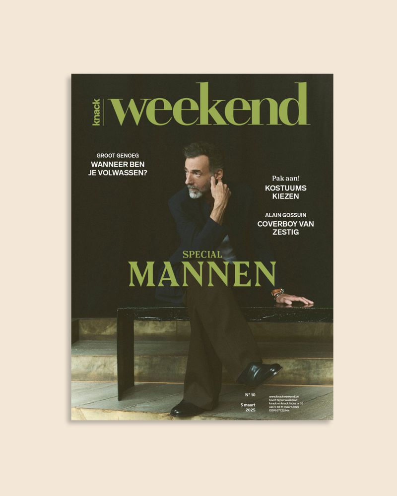 Magazine cover featuring a man in a black shirt and brown pants sitting on a bench against a dark green background and neutral-toned floor.