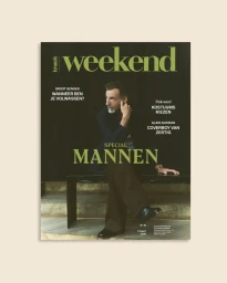 Magazine cover featuring mature man seated on a bench wearing a dark jacket and brown trousers against a dark backdrop