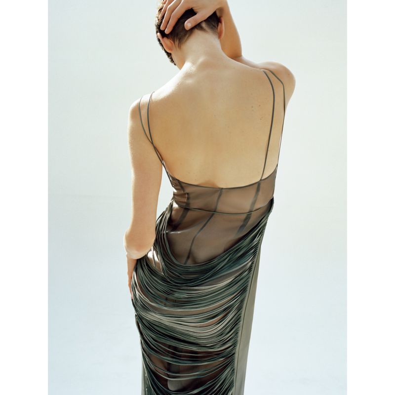 Back view of an adult female with short hair wearing a long black dress in a studio with a white background.