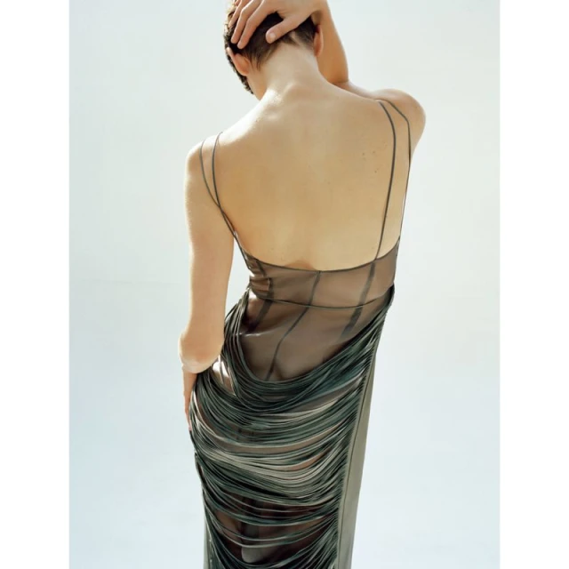 Back view of an adult female with short hair wearing a long black dress in a studio with a white background.