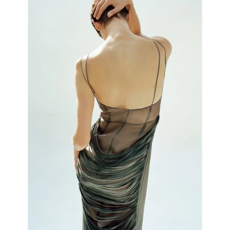 Back view of an adult female with short hair wearing a long black dress in a studio with a white background.