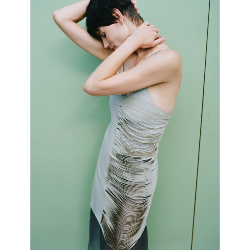 Model Saskia de Brauw wearing a fitted grey dress with a draped overlay against a green wall