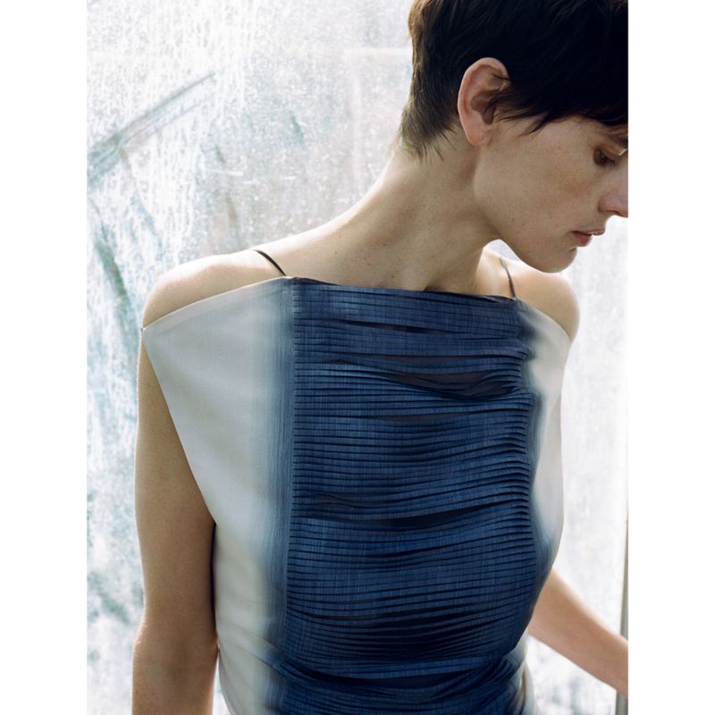 Woman in a fashionable dress poses against a textured backdrop, showcasing a blend of beauty, fashion, and minimalist editorial style.