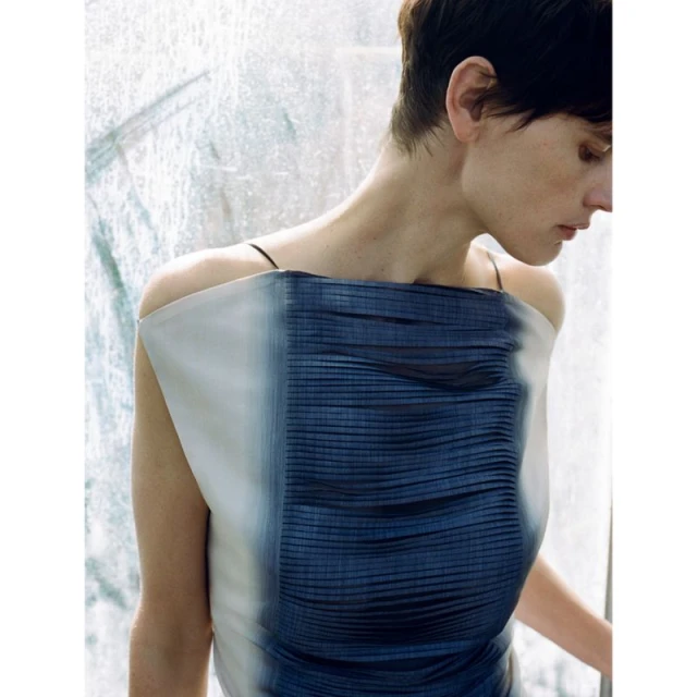 Woman in a fashionable dress poses against a textured backdrop, showcasing a blend of beauty, fashion, and minimalist editorial style.