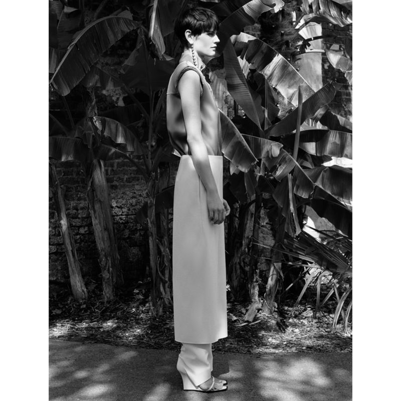 Black and white portrait of a woman in an outdoor fashion shot, wearing an outfit with a sleeveless top and wide-leg pants, standing in front of banana leaves.