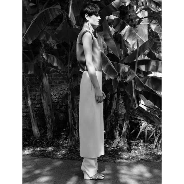 Black and white portrait of a woman in an outdoor fashion shot, wearing an outfit with a sleeveless top and wide-leg pants, standing in front of banana leaves.