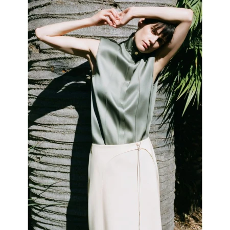 Model Saskia de Brauw in a sage green satin top and cream skirt posing against a textured tree trunk.