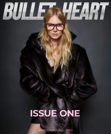 Model wearing dark tinted glasses and a plush dark coat against a plain dark grey studio background with magazine text overlays.