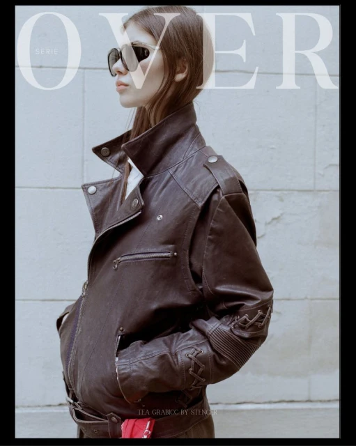 Fashion editorial shot of a woman with sunglasses and a leather jacket standing against a wall, featuring 'OVER' magazine text.